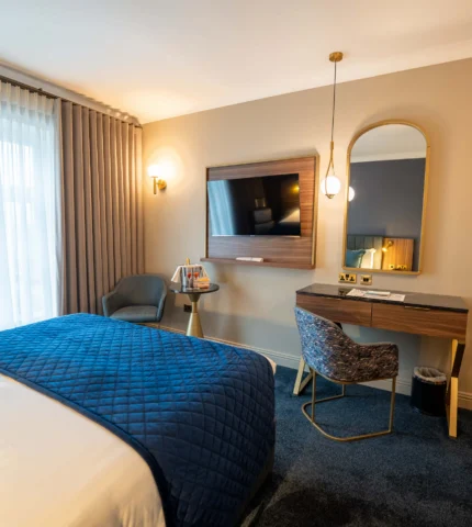 Spacious hotel room with cosy bed, elegant desk, and smart TV. Enjoy natural light and modern decor. Perfect for relaxation.