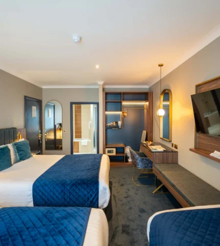 Elegant hotel room with twin beds, flat-screen TV, desk, and modern decor, offering comfort and style for a relaxing stay.