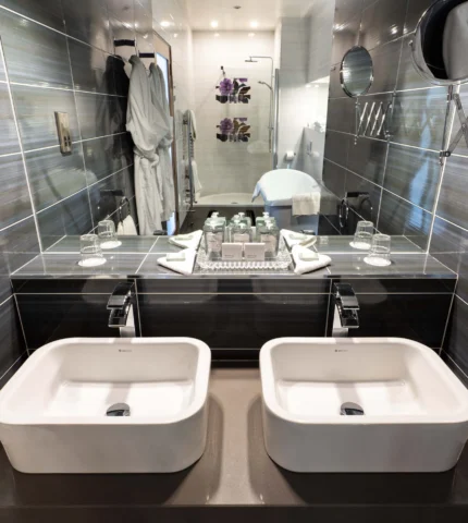 Modern luxury bathroom with double sinks, plush robes, and elegant tile design in a premium hotel suite.