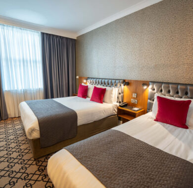 Bright hotel room with two comfy beds, plush cushions, soft lighting, elegant decor, and modern amenities.